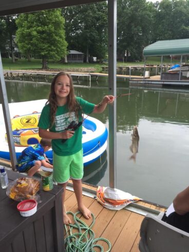 Ceili fishing from a dock beside a lake, enjoying an outdoor family activity and memorable intergenerational moments on CaringGrandparents.com.