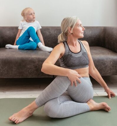Grandmother doing yoga with a young child watching on the couch, showing healthy grandparenting, family wellness, and intergenerational connection