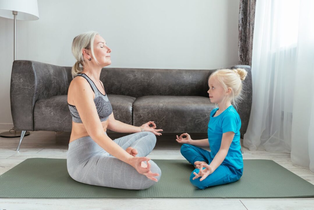 Grandmother and young girl practicing yoga together in a living room, showing grandparenting wellness, intergenerational bonding, and healthy family connection