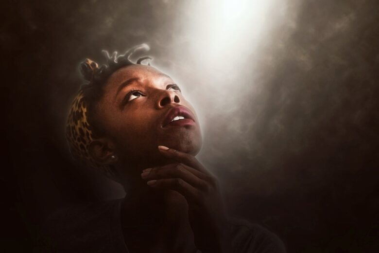 A woman lookin upward in a soft beam of light, thoughtful and hopeful, symbolizing grandparenting, faith, guidance, and family legacy.