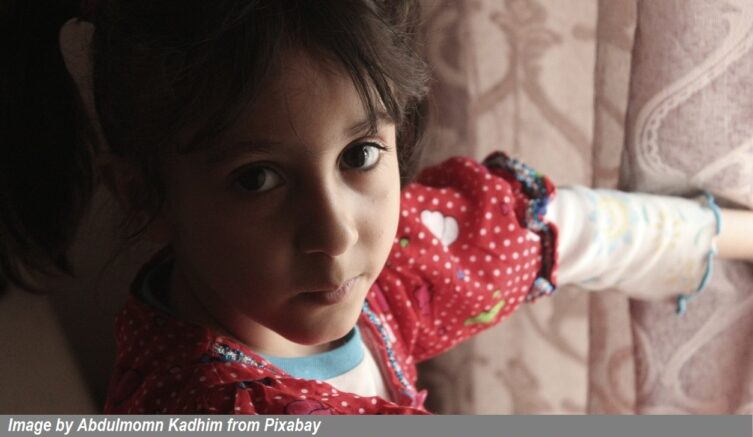 Young child in a red polka-dot shirt looking at the camera while holding a colorful handmade craft, representing childhood creativity and family activities for CaringGrandparents.com.