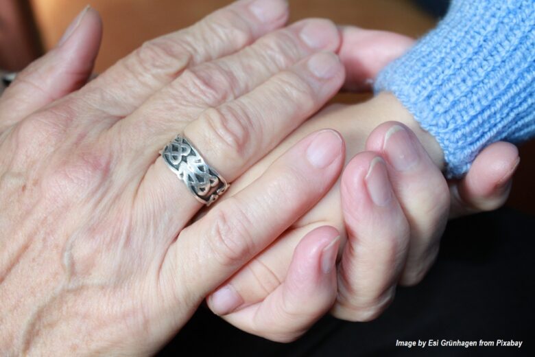 Grandparent gently holding a child’s hand, symbolizing intergenerational love, comfort, and family connection for CaringGrandparents.com.