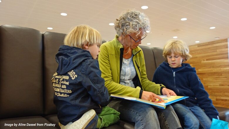 Grandmother reading a colorful book with two young grandchildren, encouraging family bonding and shared literacy in a cozy indoor setting