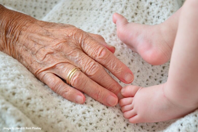 Grandparent’s hand gently touching a baby’s feet on a soft knitted blanket, symbolizing intergenerational love, family connection, and caring grandparents.