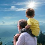 Grandfather carrying his grandson on his shoulders while enjoying a scenic mountain overlook, celebrating intergenerational bonding and outdoor family time.