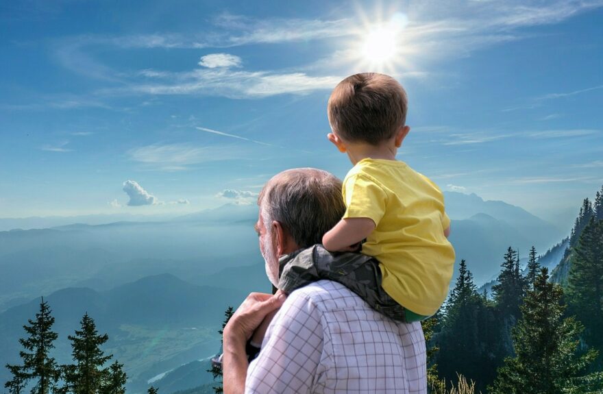 Grandfather carrying his grandson on his shoulders while enjoying a scenic mountain overlook, celebrating intergenerational bonding and outdoor family time.
