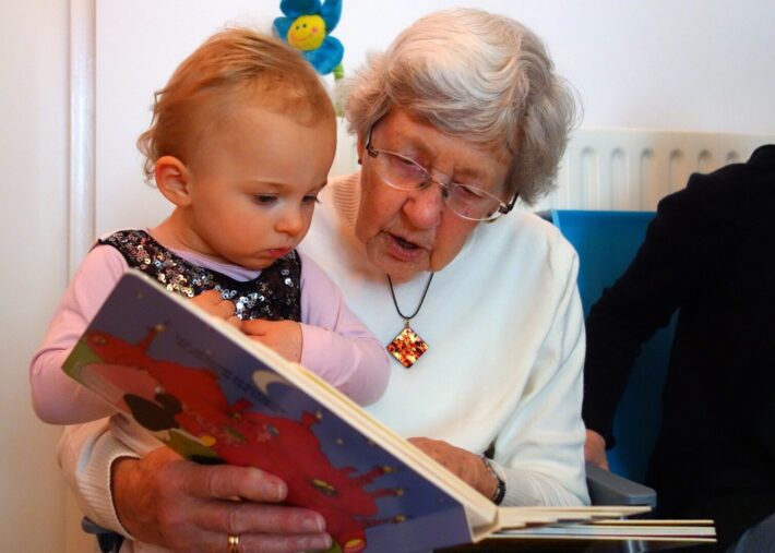Grandmother reading a colorful picture book with her young granddaughter, encouraging early literacy and meaningful intergenerational bonding.