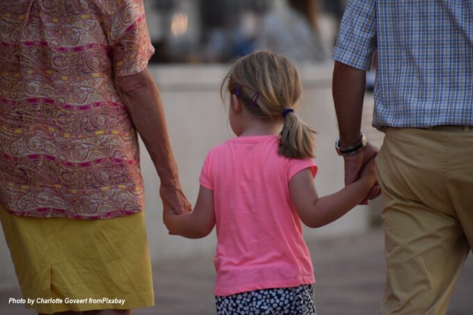 Grandparents holding hands with their granddaughter while walking together, illustrating loving intergenerational family bonding and quality time.