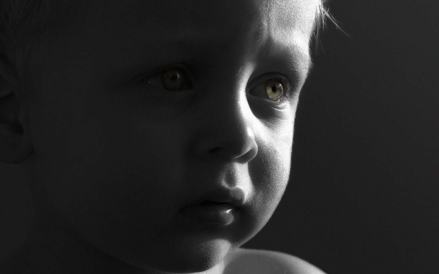 Black-and-white close-up portrait of a young child looking thoughtfully toward the light, illustrating childhood innocence and family caregiving.