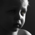 Black-and-white close-up portrait of a young child looking thoughtfully toward the light, illustrating childhood innocence and family caregiving.