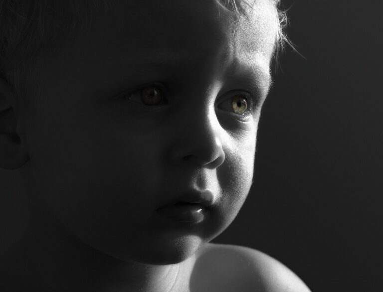 Black-and-white close-up portrait of a young child looking thoughtfully toward the light, illustrating childhood innocence and family caregiving.
