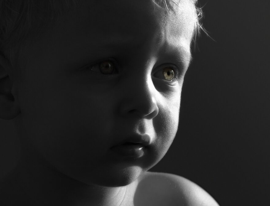 Black-and-white close-up portrait of a young child looking thoughtfully toward the light, illustrating childhood innocence and family caregiving.