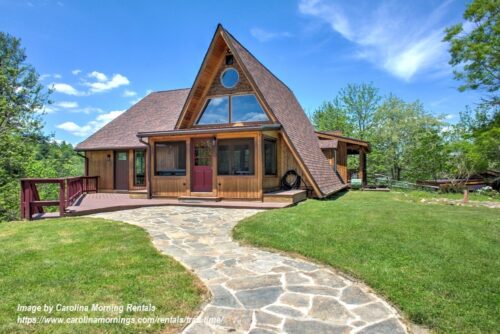 Rustic A-frame vacation cabin with a stone walkway, covered porch, and green lawn in a