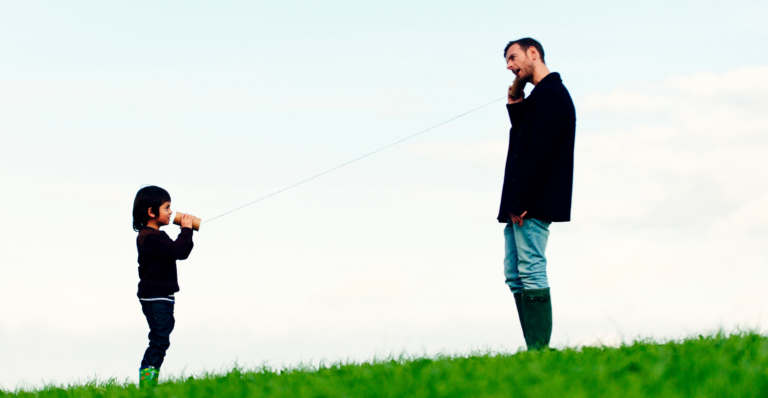 Grandparent and grandchild talking with a tin can string telephone outdoors on a grassy hill