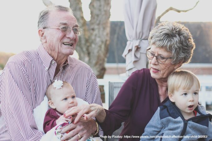 Loving grandparents spending time with their grandchildren outdoors, holding a baby and cuddling a young boy