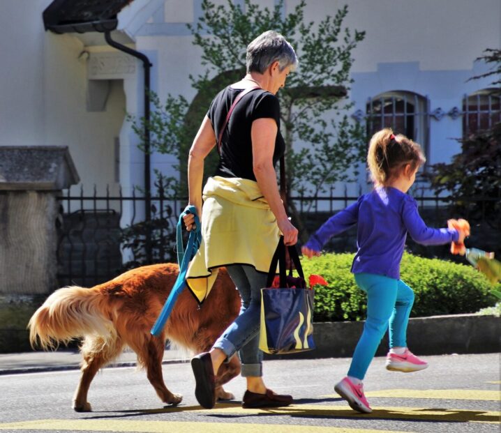 Grandmother walking with her granddaughter and dog on a sunny neighborhood sidewalk
