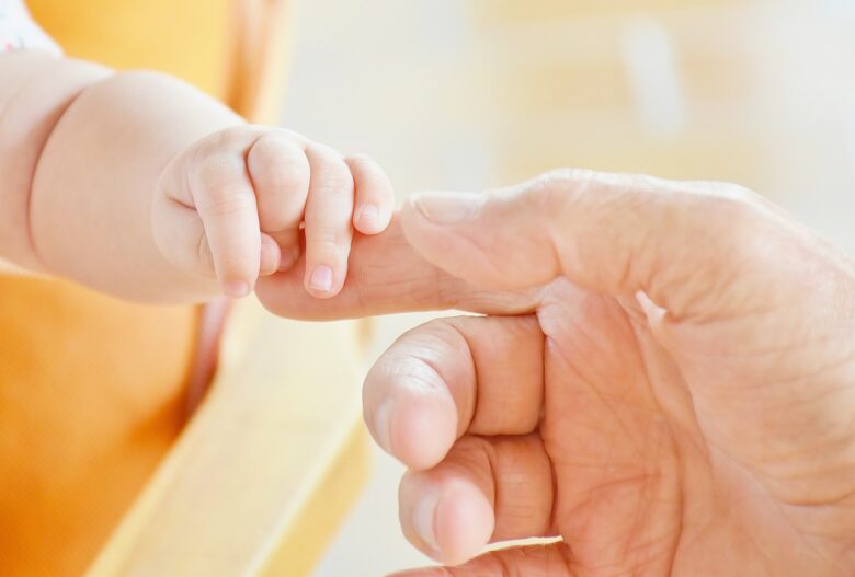 Grandparent and baby holding fingers, symbolizing intergenerational connection, grandparenting love, and a caring family bond.