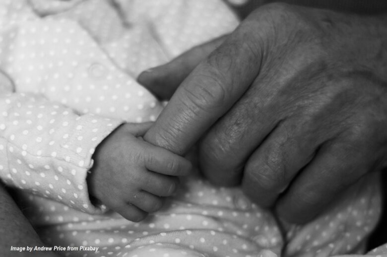 Black-and-white photo of a newborn baby holding a grandparent’s hand, symbolizing the loving bond between generations.