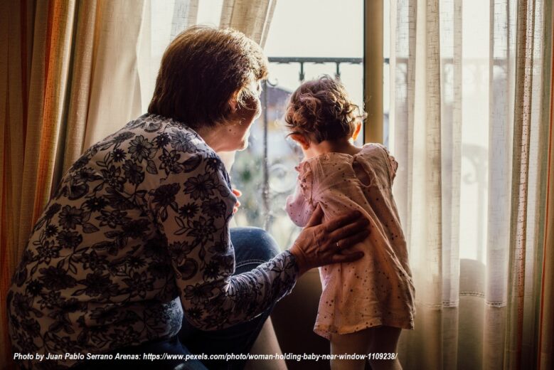 Older woman gently holding a toddler by the window, showing grandparenting, caregiving, and a loving intergenerational family moment.