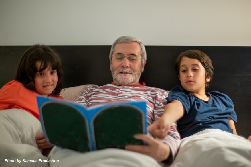 Grandfather reading a bedtime story with two grandchildren, showing loving grandparenting, family bonding, and shared learning across generations.