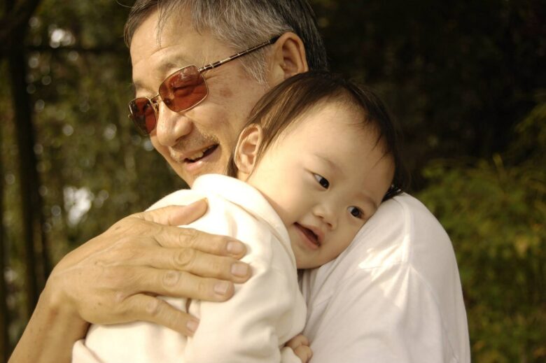 Older grandfather holding a young child outdoors, showing intergenerational family love, grandparenting care, and a warm family bond.