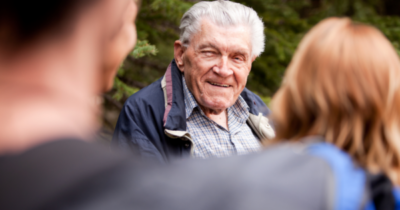 Smiling elderly grandfather talking with family outdoors, a warm multigenerational grandparenting moment.