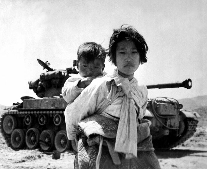 Black and white historic photo of a young woman carrying a child in front of a tank, symbolizing family survival, war hardship, and the protective legacy themes often used in grandparenting