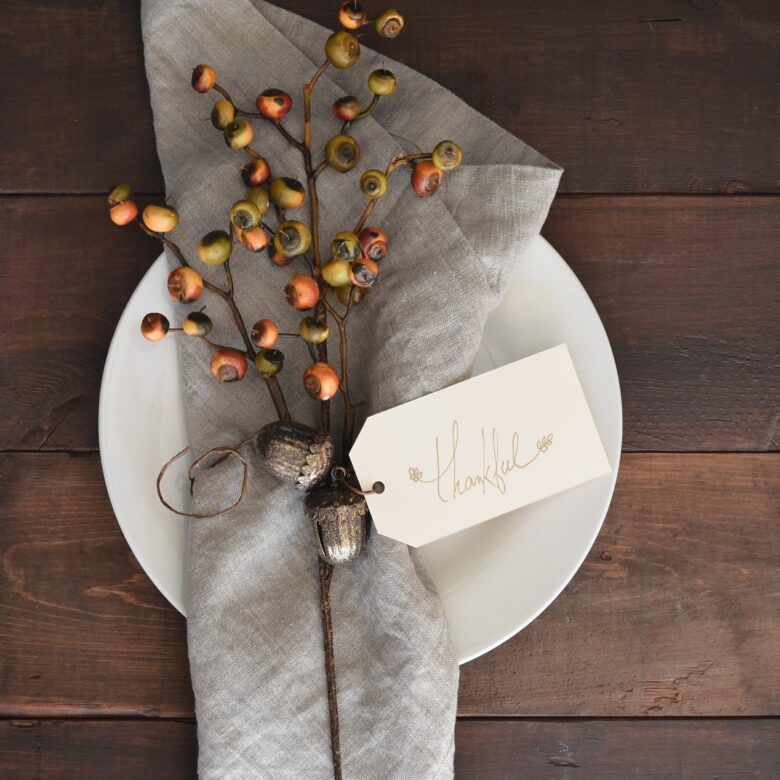 Decorative Thanksgiving place setting with a thank you tag and autumn berry branch, symbolizing family gratitude, grandparenting, and intergenerational celebration.
