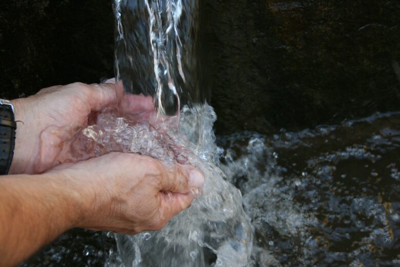 Hands collecting fresh water from a stream, symbolizing care, nourishment, and the flow of grandparenting wisdom.