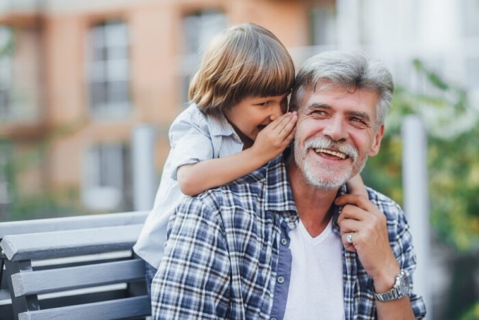 Grandfather and young grandson sharing a playful whisper on a bench, illustrating warm grandparenting, intergenerational bonding, and family joy