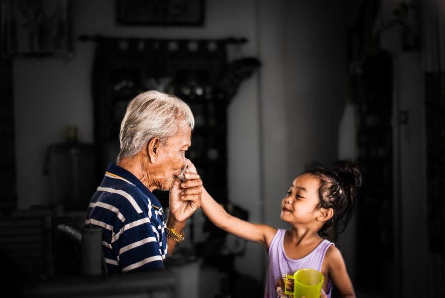 Grandfather and young granddaughter sharing a tender moment indoors, showing intergenerational family bonding, care, and grandparenting