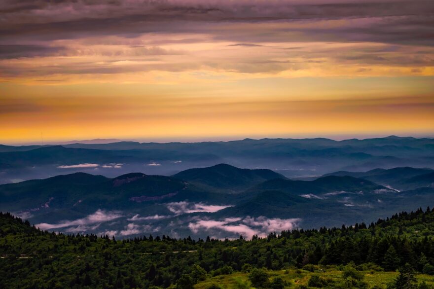 A dramatic mountain landscape at sunrise with layered ridges, mist in the valleys, and a warm golden sky, creating a peaceful backdrop for grandparenting content.