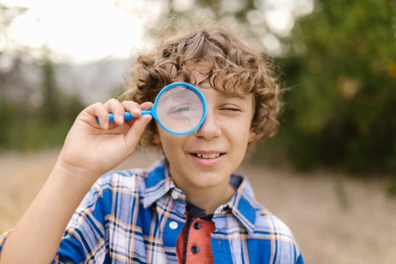 Young boy holding a magnifying glass to his eye outdoors, showing curiosity, play, and intergenerational learning in grandparenting