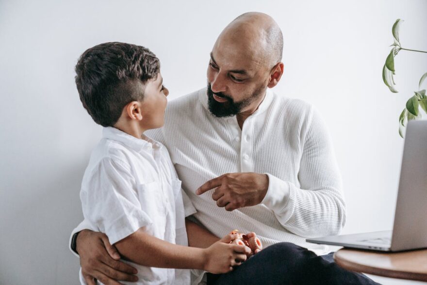 Older father or grandfather talking with young boy indoors, showing intergenerational grandparenting, family guidance, and close emotional connection