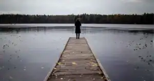 A woman standing on an unfinished brdige over a lake.