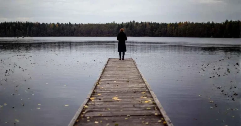 A woman standing on an unfinished brdige over a lake.