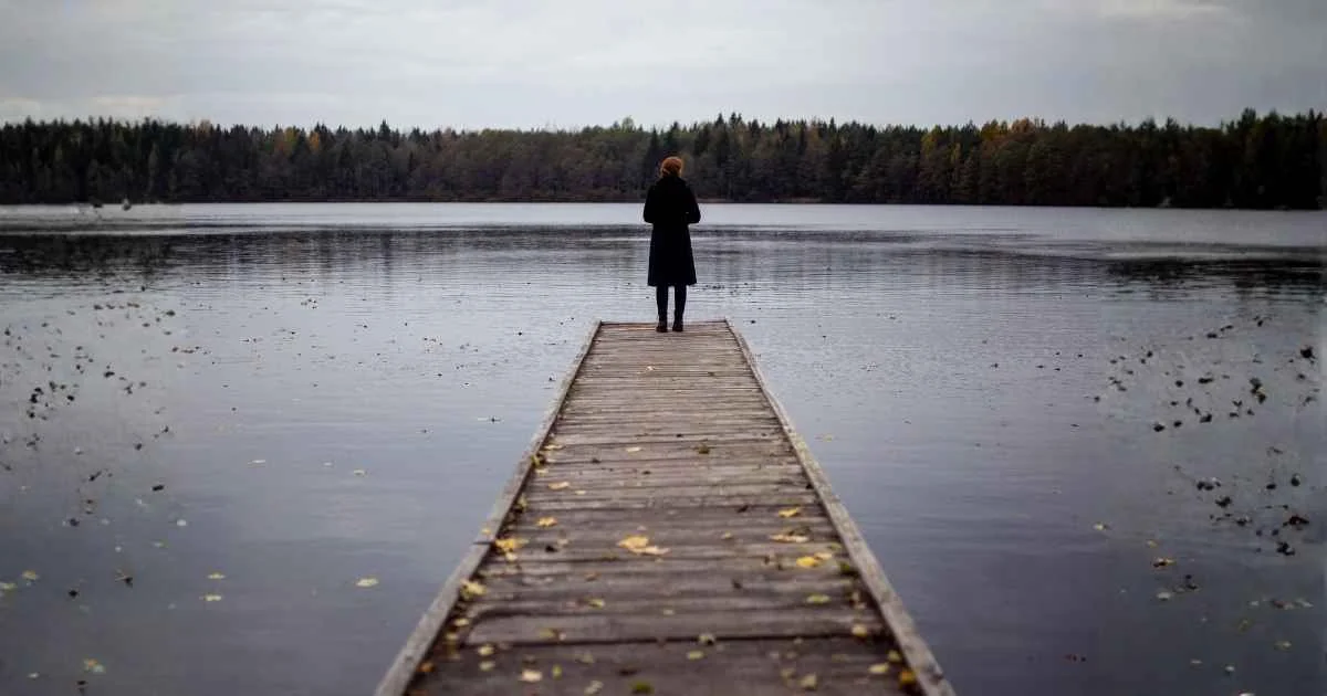 A woman standing on an unfinished brdige over a lake.